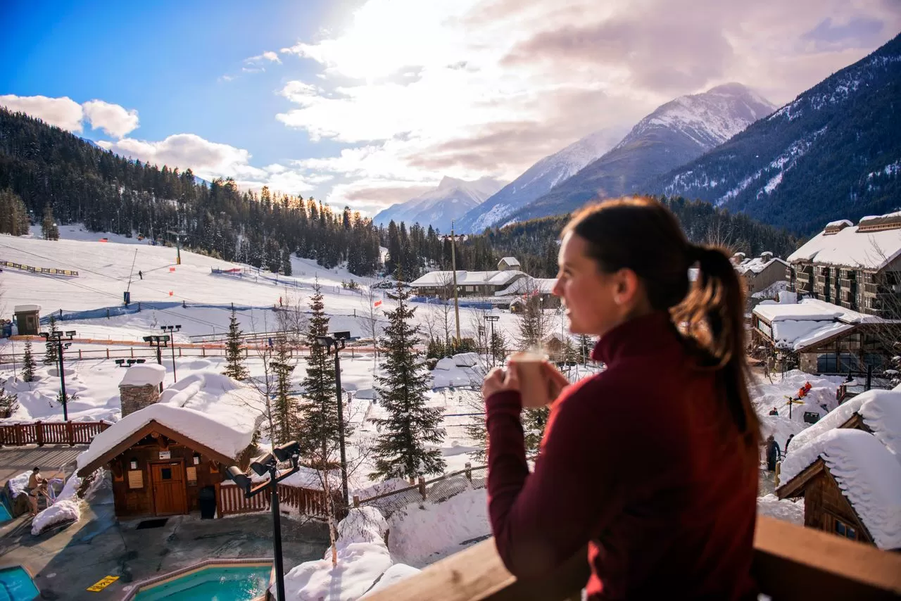 Panorama Mountain Resort springs lodge and pools. A lady enjoying a hot beverage on the deck overlooking the resort.